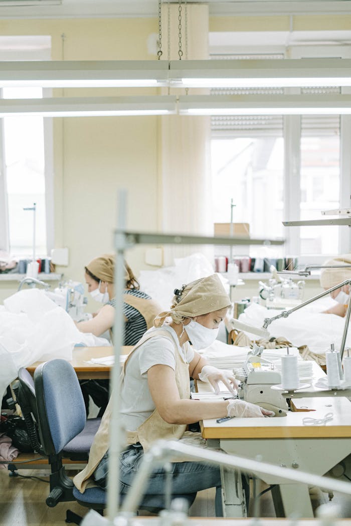 Women working at sewing machines in a textile factory wearing protective masks.